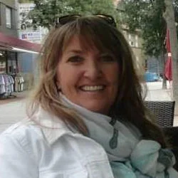 A woman wearing a white jacket and scarf sitting at an outdoor table.