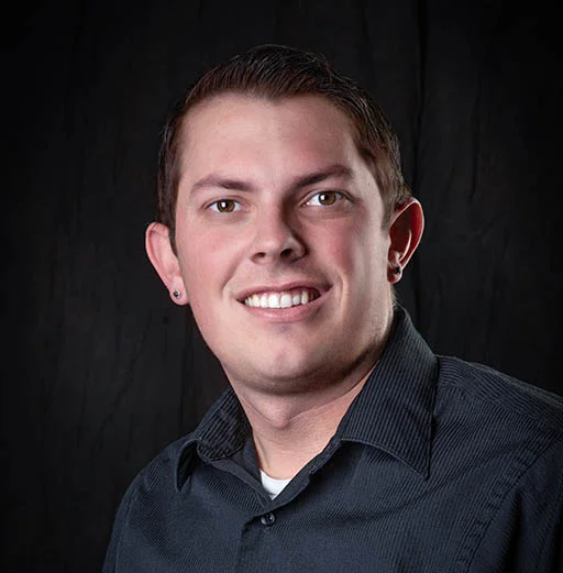 A man in a black shirt smiling in front of a black background.